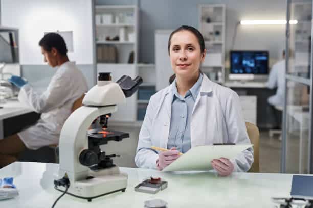 une femme scientifique regarde une caméra travaillant avec un microscope en laboratoire - recherche et développement photos et images de collection